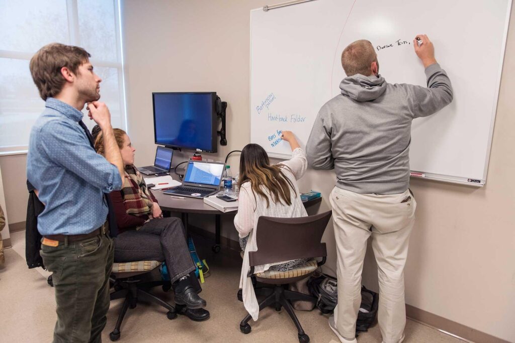 Picture of students in a classroom writing on the whiteboard.